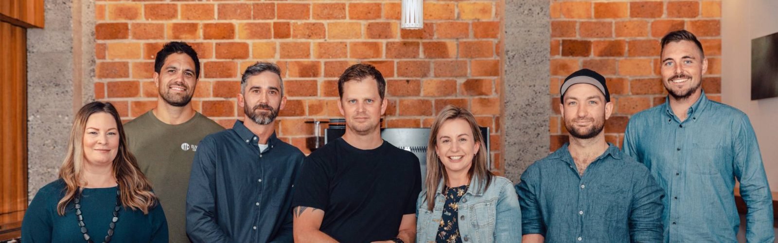 The OTC team standing in front of a rustic brick backdrop